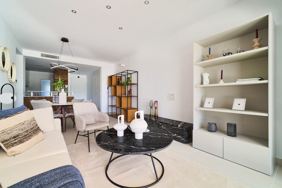 LOS MIRADORES DEL SOL with a seating area, round black marble coffee table, built-in open wall shelving with decorative objects and a dining area in the background.