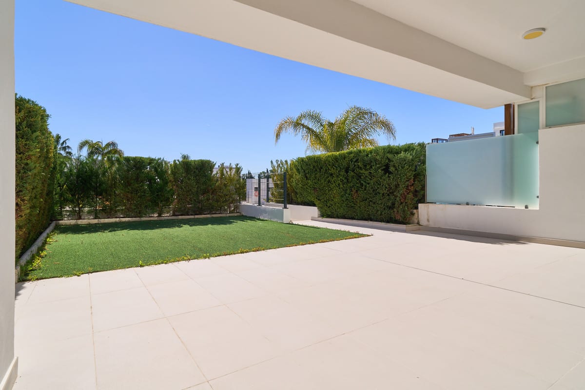 LOS MIRADORES DEL SOL with a covered tiled terrace, green lawn, tall hedges, palm trees and a frosted glass screen.