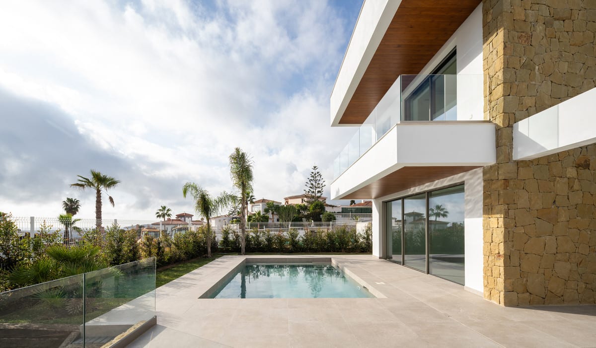 Side view of the terrace and pool, with natural stone, a glass balustrade on the projecting volume and timber details beneath the overhangs.