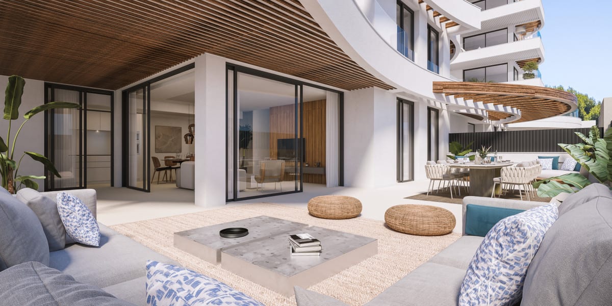 Project visualisation of MARINA GOLDEN BAY featuring a spacious outdoor area, a grey lounge sofa with blue cushions, a low marble coffee table, rattan pouffes, sliding glass doors to the interior and a curved wooden slatted ceiling.