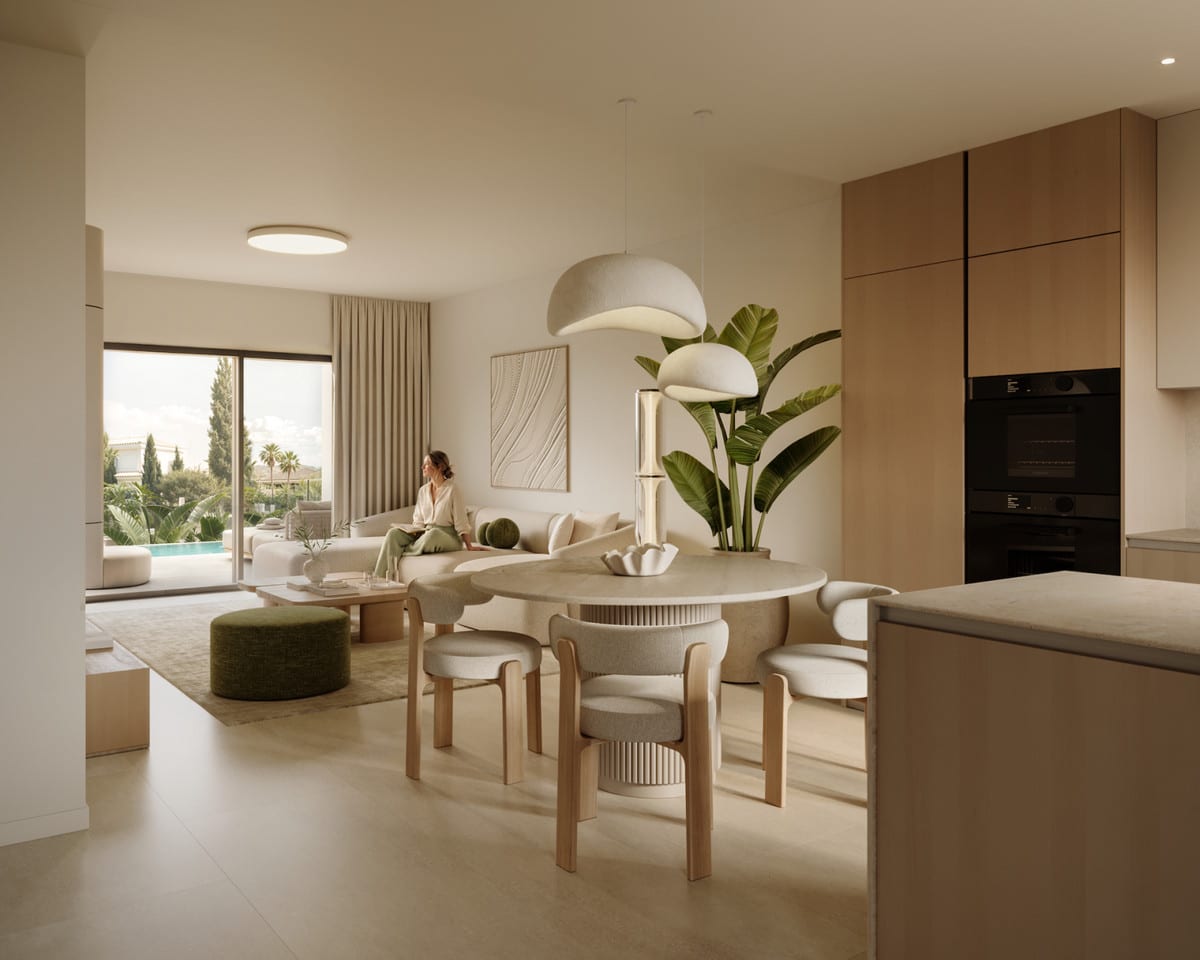 Project visualisation of MARTAGINA HILLS featuring an open-plan living space: a light-wood kitchen unit with an integrated oven, a round dining table with light-wood chairs, a large pendant light, a cream sofa and sliding glass doors overlooking an outdoor area with a pool.