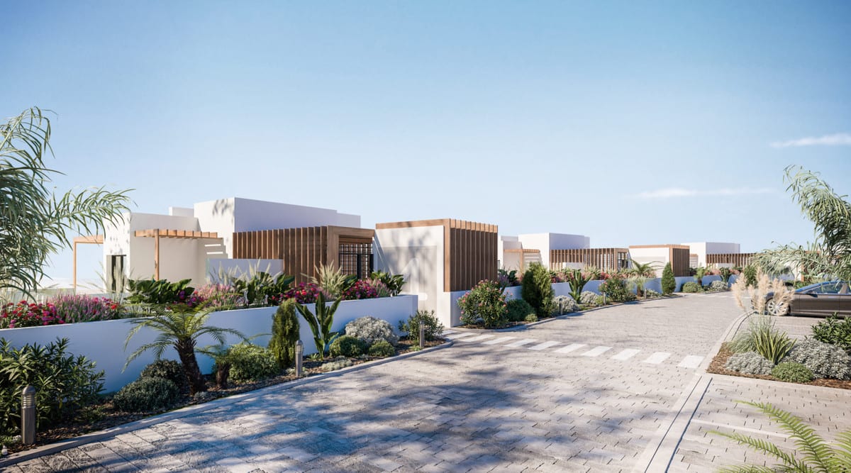 Project visualisation of MIRADOR DE ESTEPONA HILLS with a paved driveway alongside low white buildings, vertical wooden façade accents and flowering planting.