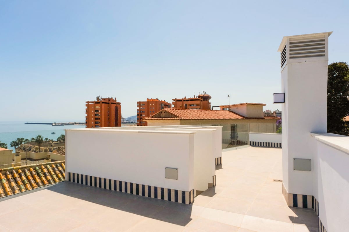 MONTE SANCHA 28 photographed on the empty roof terrace with light tiles, white walls with a decorative blue-and-white tiled border, glass balustrade and views of surrounding buildings and the sea.
