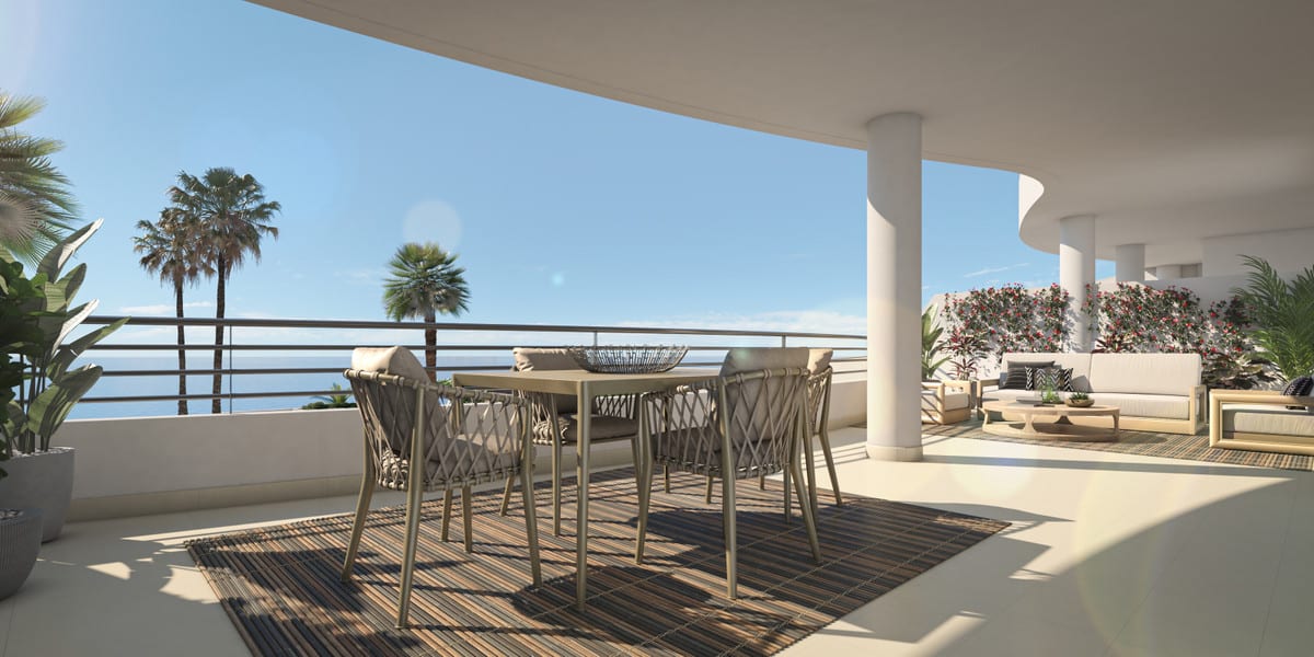 Project visualisation of NEXUS RESIDENCES with a covered terrace, a dining table with wicker chairs, a lounge seating area, a white round column, palm trees and sea views in the background.
