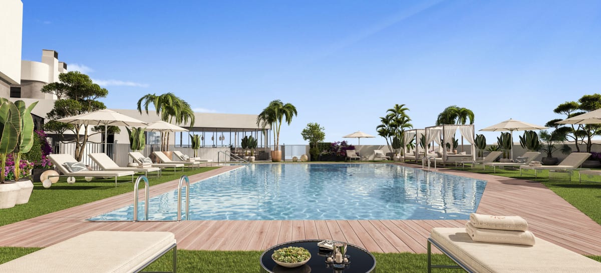 Project visualisation of ORIGIN featuring a rectangular outdoor swimming pool on a sunny day, surrounded by a green lawn, wooden decking, sun loungers with parasols, curtained daybeds and palm trees.