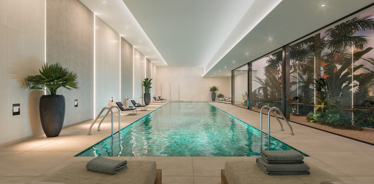 Project visualisation of ORIGIN featuring a long indoor swimming pool, light beige tiled flooring, recessed ceiling lighting, large planters, sun loungers and a glass wall with tropical planting outside.