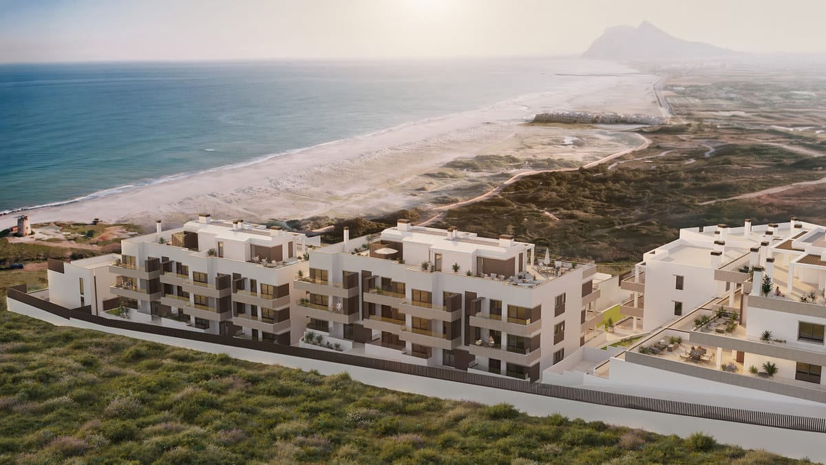 Aerial project visualisation of PARAISO BEACH with cream-coloured residential buildings featuring terraces, adjacent dune landscape, sandy beach and sea, with a rocky hill in the distance.