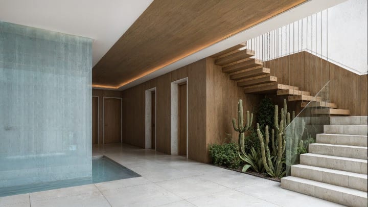 Project visualisation of the entrance hall at PARAISO DE AZAHAR with light tiled flooring, wooden wall panelling, a floating staircase with a glass balustrade and cacti as green accents.