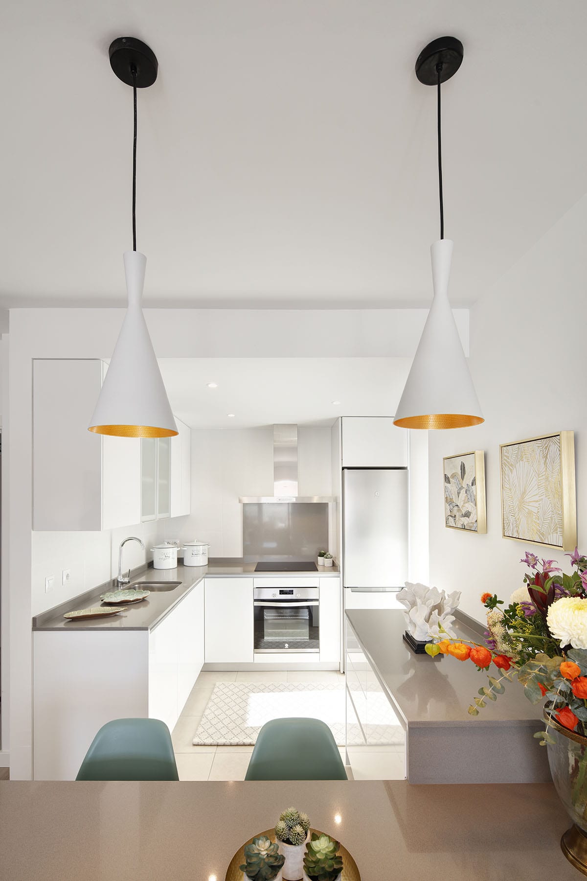 Detailed view of the kitchen at RESIDENCIAL ALBATROS XIV with white cabinetry, grey worktops, integrated oven, stainless-steel fridge, extractor hood and two white pendant lights with gold interiors.