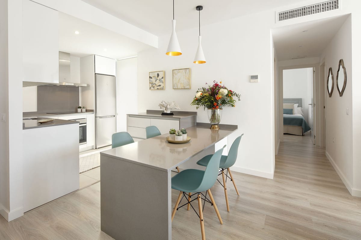 Open-plan kitchen and dining area at RESIDENCIAL ALBATROS XV with white cabinetry, grey worktop, kitchen island and four mint-green chairs beneath white pendant lights with gold interiors.