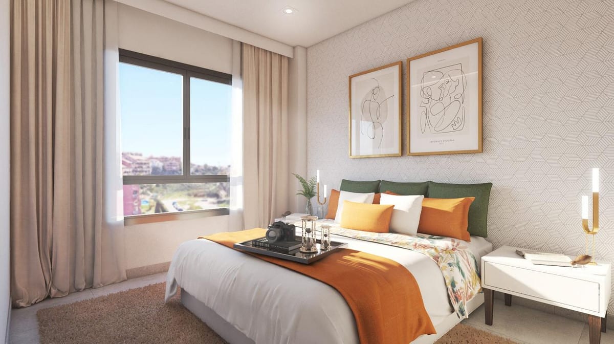 Development visualisation of RESIDENCIAL SUNHILL featuring a bedroom with a double bed, green headboard, orange and yellow cushions, white bedside table, two framed artworks above the bed and a large window with beige curtains.