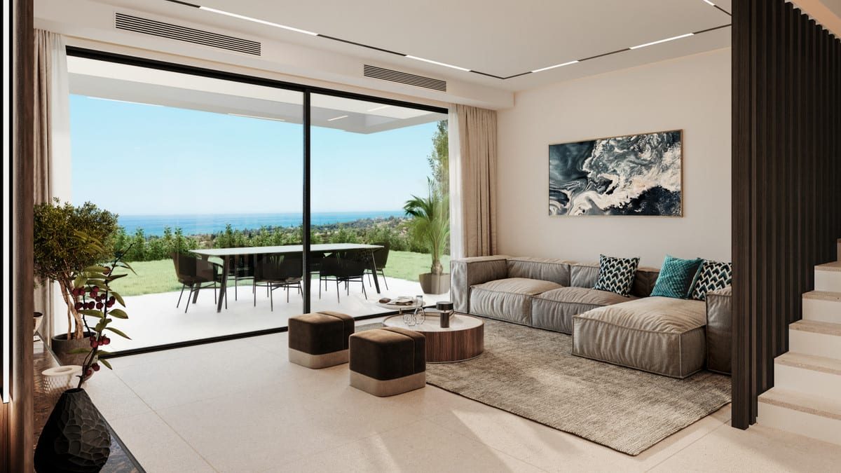Rendered interior visualisation of SERENITY HILLS with a grey seating area, brown ottomans, large floor-to-ceiling glass sliding doors opening onto a terrace with a dining table and chairs, a lawn and sea views on the horizon.