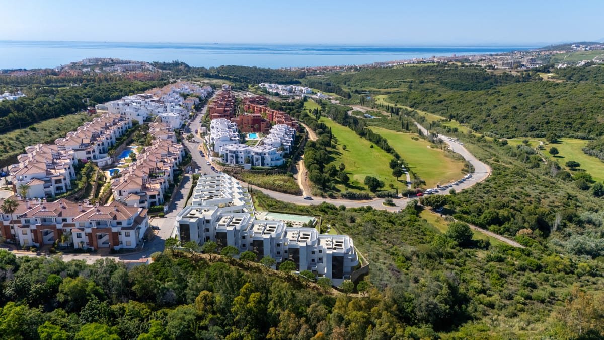 Aerial photograph of white buildings, green hills and the sea on the horizon.