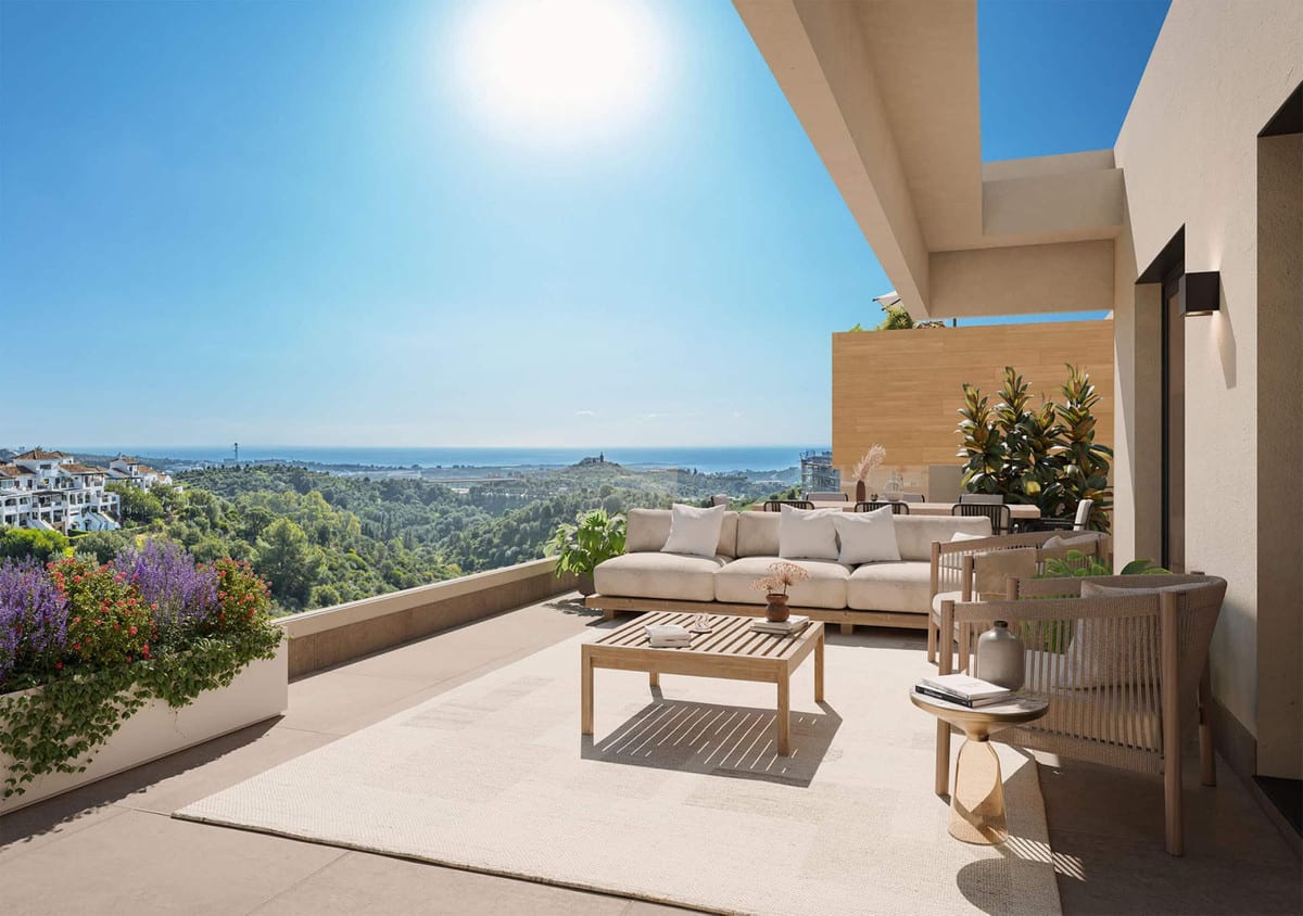 Project visualisation of SOLEIL featuring a spacious terrace, pale sofa, wooden coffee table, woven chairs, planters with colourful planting and expansive views over greenery and the sea.