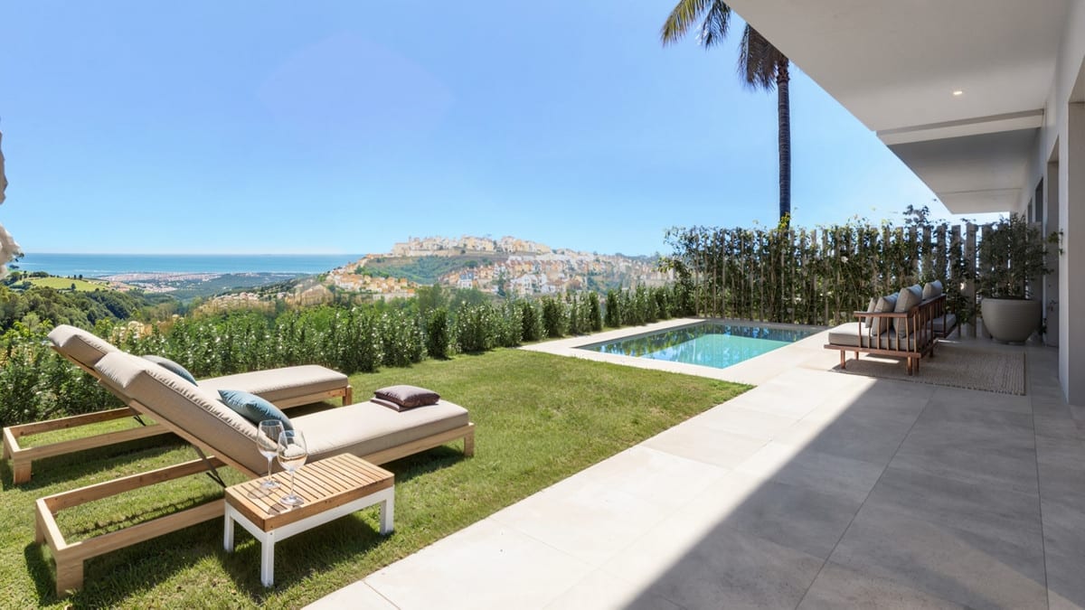 Rendered outdoor space with swimming pool, sun loungers and an open view towards a hilltop town and the sea in the background.