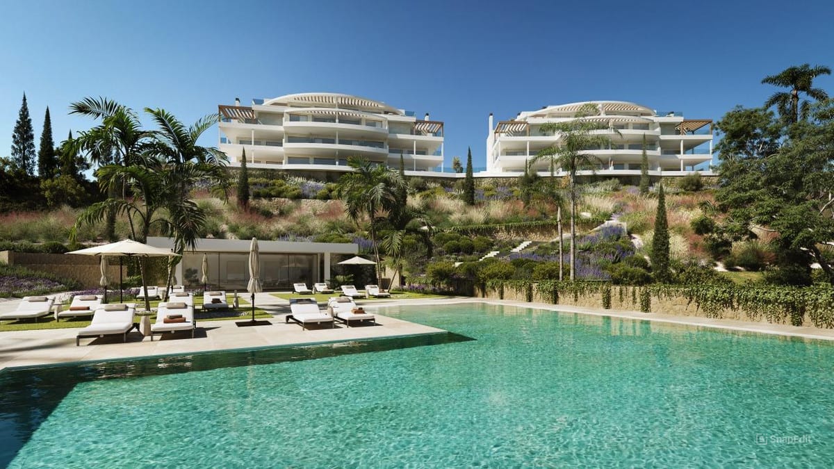 Project visualisation of THE EAGLE RESIDENCES with a turquoise swimming pool in the foreground, rows of sun loungers with parasols, palm trees and two white buildings with curved façades on a landscaped hillside in the background.