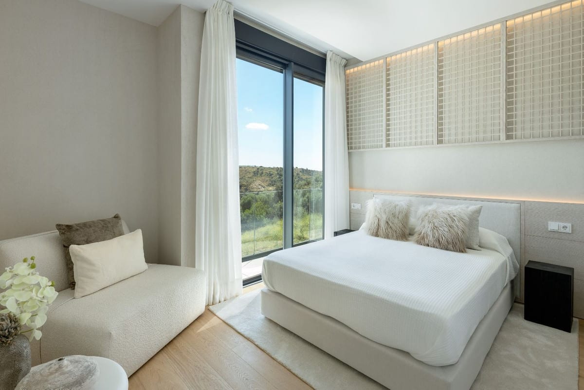 THE LIST RIO REAL with a double bed, light chaise longue, glazed sliding door with glass balustrade, white curtains and illuminated wall panels above the headboard.