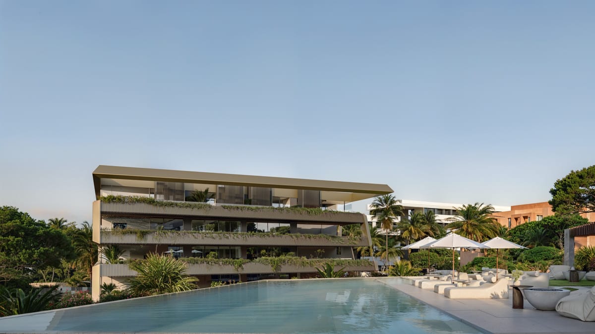 Project visualisation of THE PRIVILEGE with a wide swimming pool, white lounge furniture and parasols in front of a building with planted balconies and surrounding greenery.