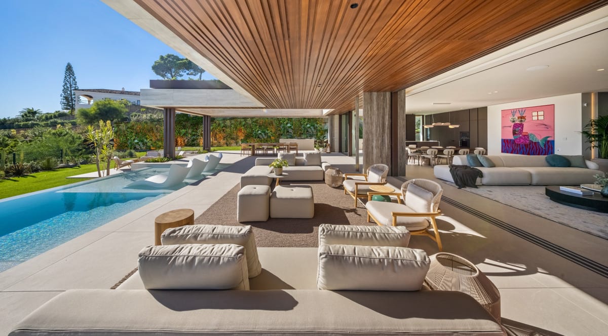 Covered terrace of THE SKY MARBELLA VILLAS in daylight, with lounge seating beside the pool and an open connection to the living and dining areas.
