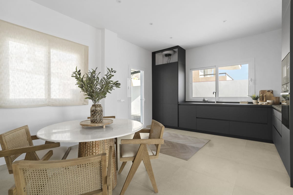 URBANIZACIÓN OLIMPO kitchen with a wall of dark cabinets, a round table with a white marble top, wooden chairs with woven backrests and a window with a linen roller blind.