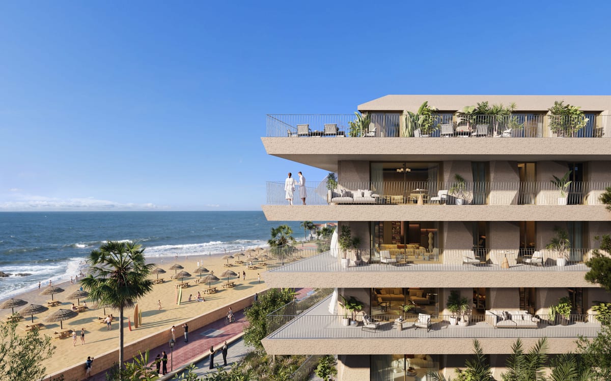 Rendered façade visualisation of VESTA MARE with several wide terraces featuring seating and planting, two figures on the upper balcony, and a beach with straw parasols and the sea visible in the left background.