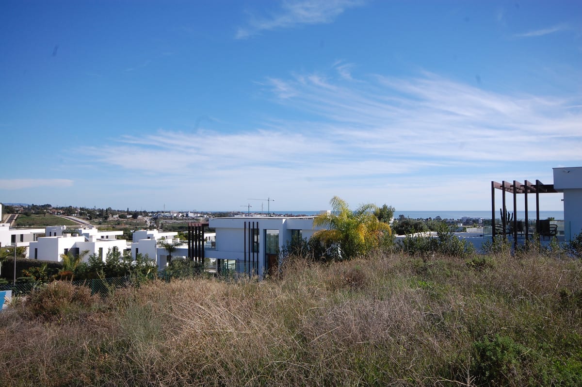 Photograph of the surroundings of VILLA AZAHAR PRIVÉ, with dry vegetation, white buildings, palm trees and the sea on the horizon.