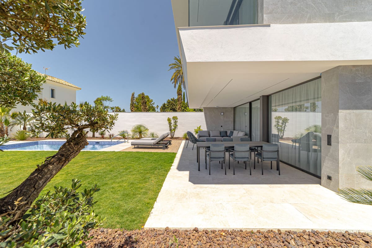 View of the covered terrace with a dining table and seating beside the lawn and pool.
