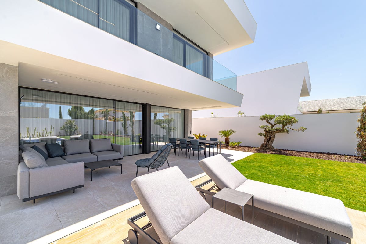 View of the terrace with sun loungers, a sofa and a dining area beside the garden.