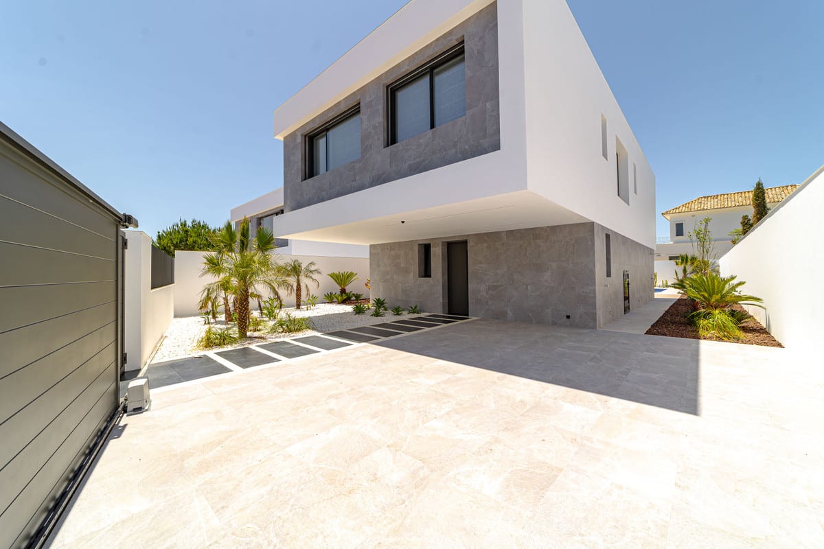 View of the villa entrance with a paved driveway, sliding gate and planting.
