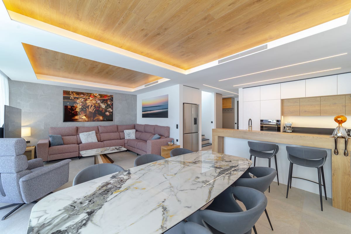 View of an open living and dining area with a kitchen and wooden breakfast bar.