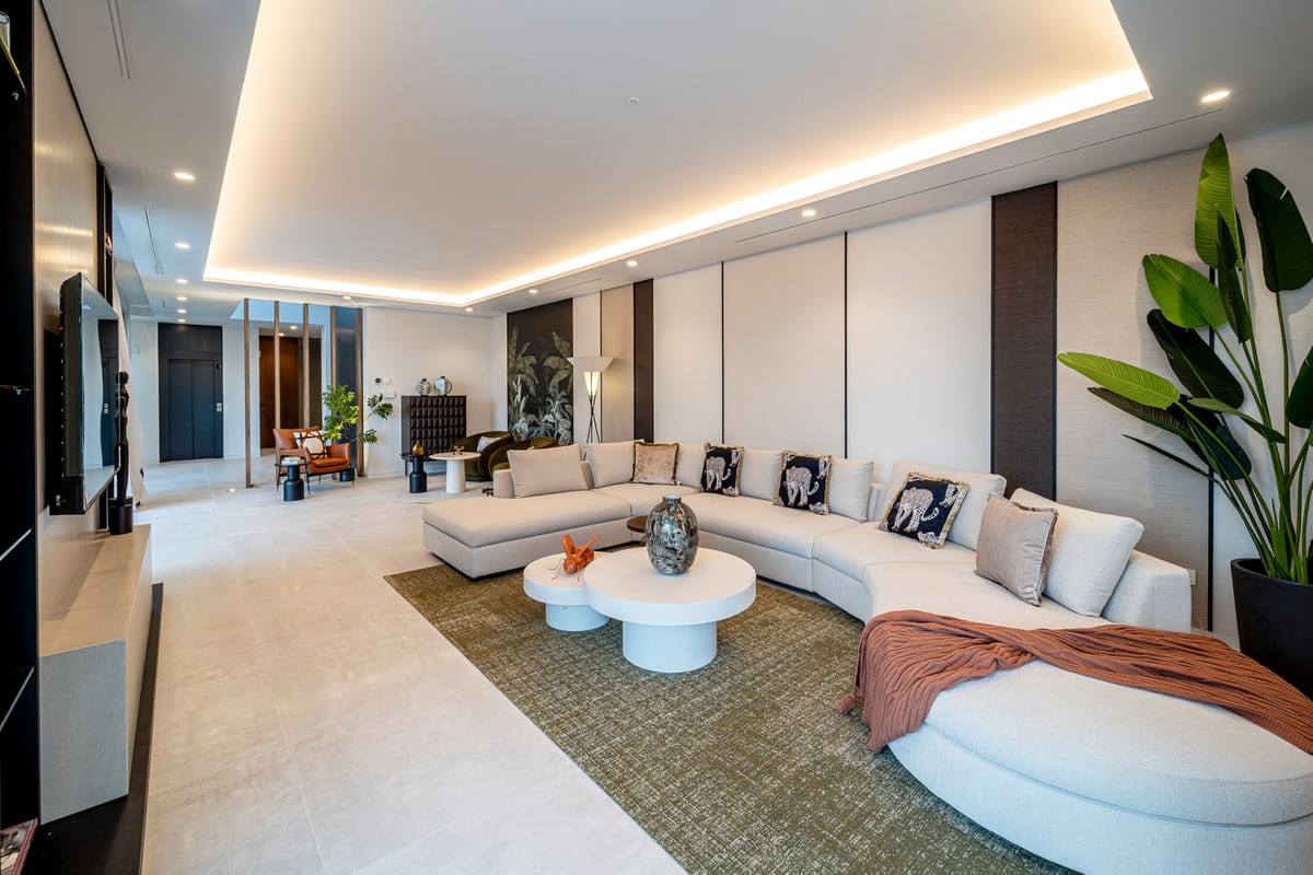 Living room of VILLA ESMERALDA with a curved light-coloured sofa, round coffee tables and a large indoor plant.