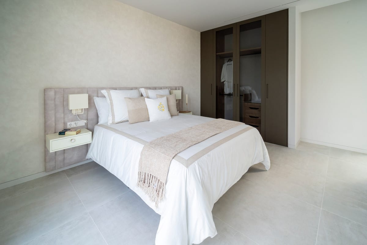 Bedroom of VILLA ESMERALDA in beige and white tones, with a wardrobe with glazed doors and a light tiled floor.