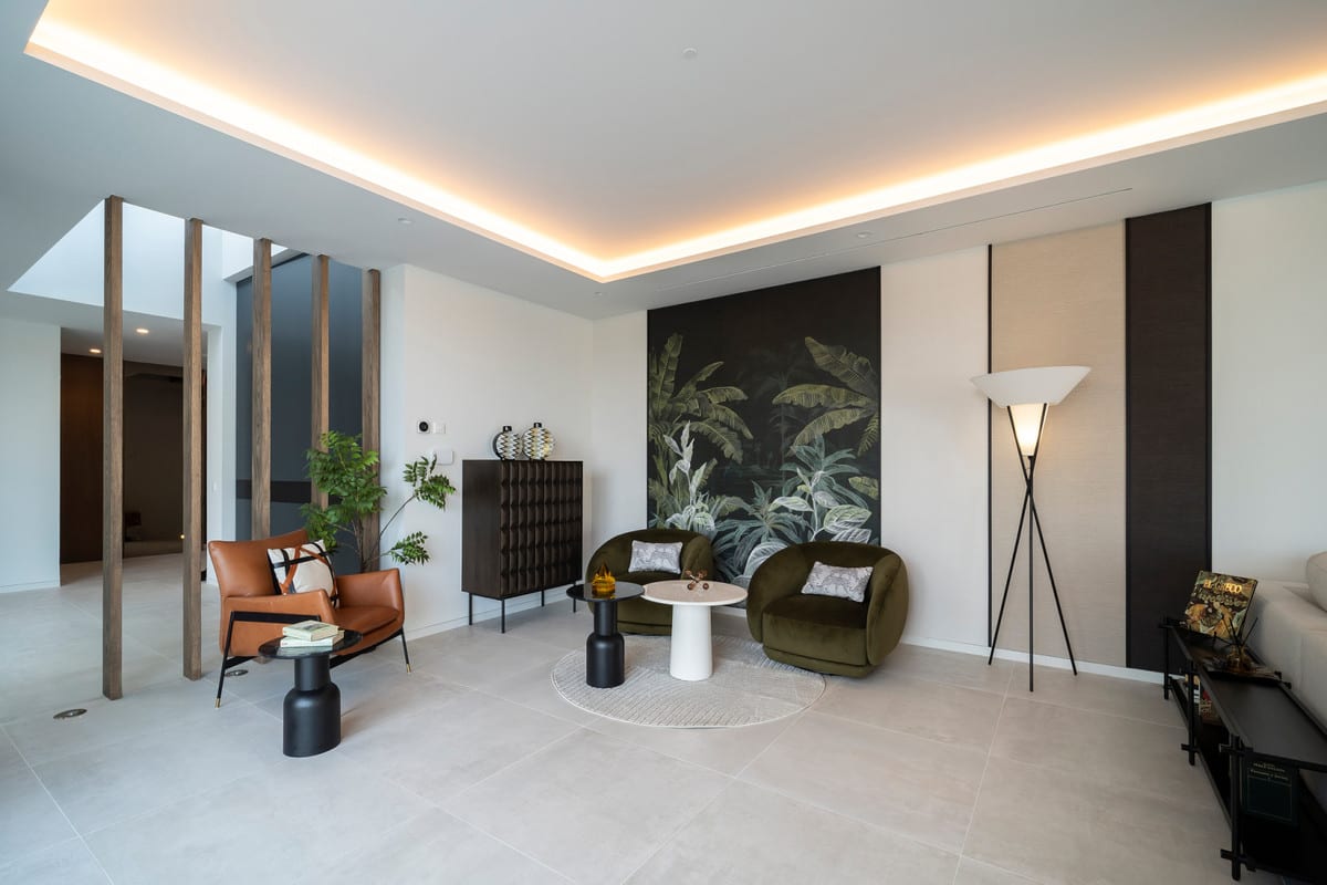 Seating area in VILLA ESMERALDA with a leather armchair, two green chairs, botanical wall decoration and timber room dividers.