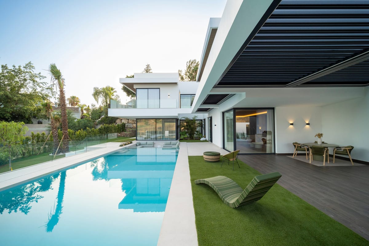 Poolside terrace of VILLA ESMERALDA with a green lounger and a covered dining area beneath a louvred pergola.