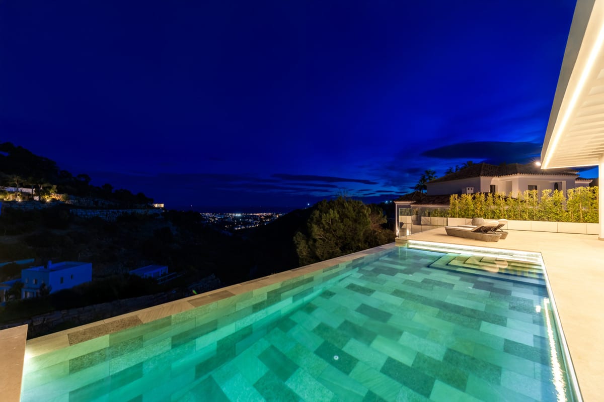 Illuminated pool of VILLA OMEGA at night, with distant lights visible beyond the surrounding hills.