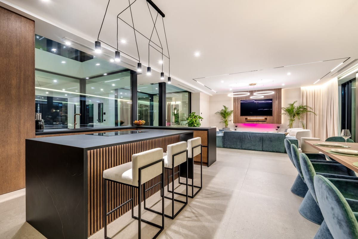 Open living space of VILLA OMEGA combining a kitchen island with bar seating, dining area and lounge.
