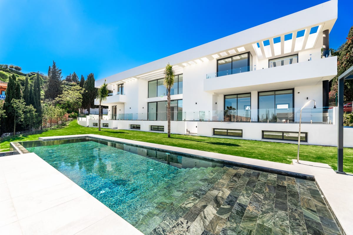 The white facade with broad windows overlooks the pool, lawn and surrounding planting.