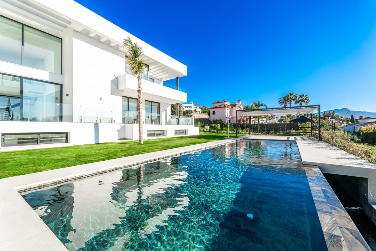View along the pool towards the pergola, with the modern facade and terraces on the left.