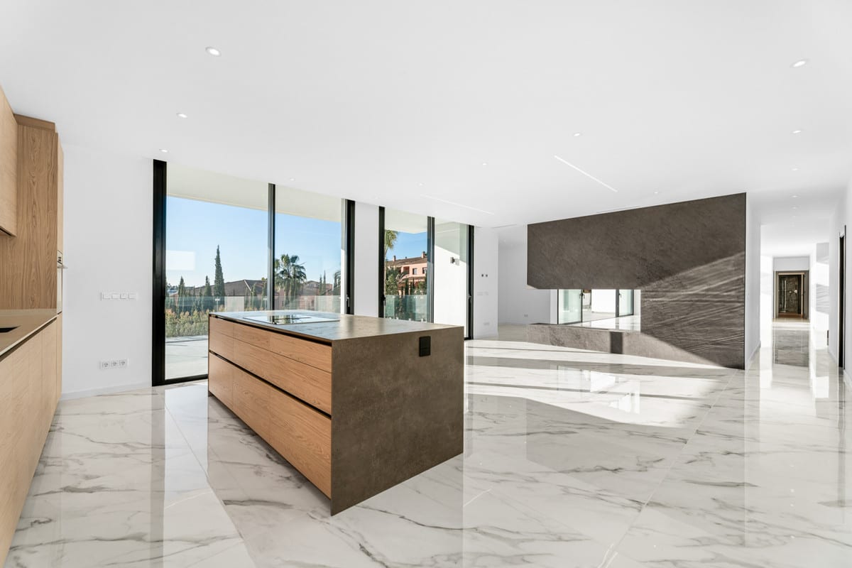 The kitchen island stands at the centre of the bright space, where a dark wall contrasts with the white floor.