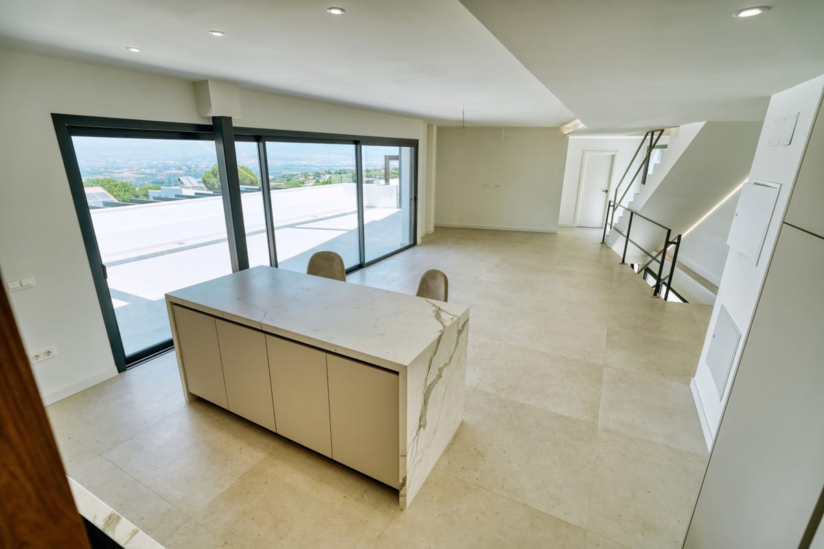 VILLA SANTHAI 3 Y 9 open-plan living space with a veined marble kitchen island, light tiled flooring, wide sliding doors and staircase with dark steel balustrade