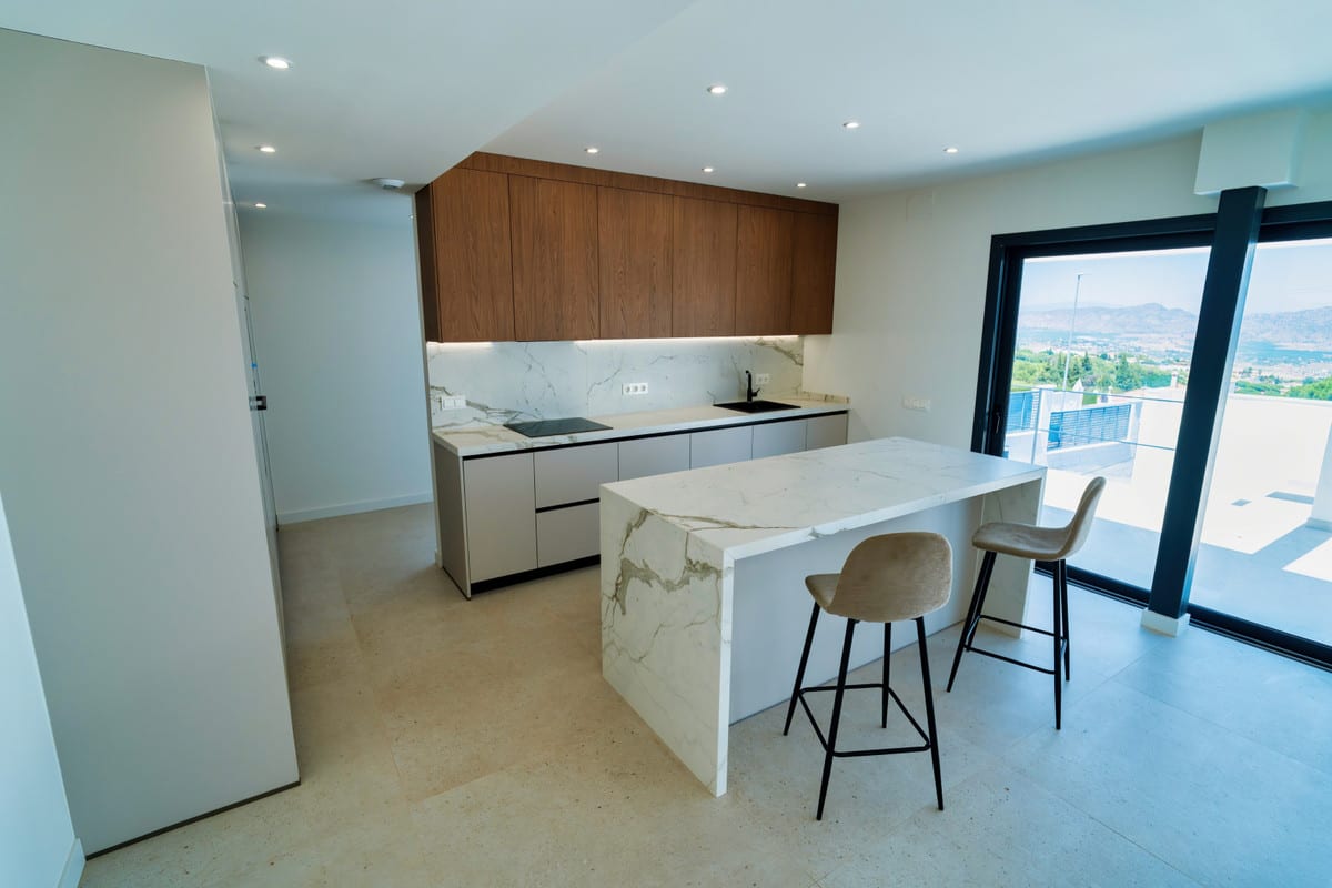 VILLA SANTHAI 3 Y 9 kitchen with wooden wall cabinets, veined marble splashback and island with two beige bar stools