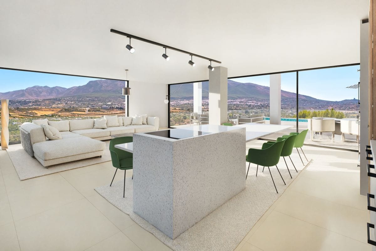 Photorealistic interior visualisation of VISTA DEL REY EVIDENT with a light terrazzo kitchen island, green chairs around the island and dining table, a cream corner sofa, black track lighting and large black-framed windows with mountain views.