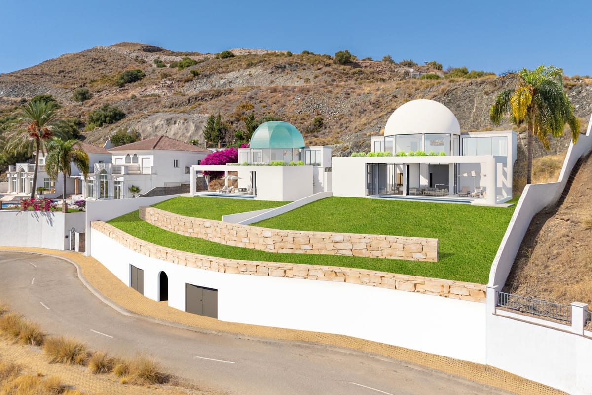 Project visualisation of VISTA DEL REY MIA&AIM from an oblique angle, with two white buildings, a turquoise glass dome and a white dome, expansive glazing, sloping lawns and a road along the front.