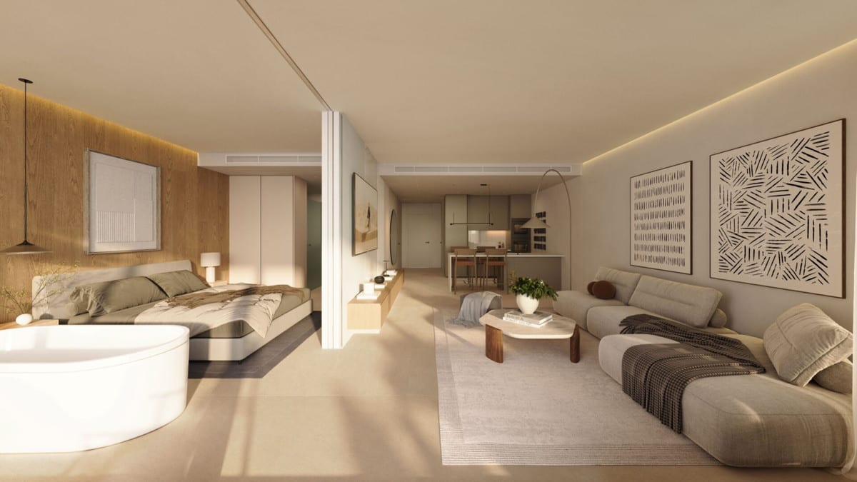 Project visualisation of WATERFALL RESIDENCES with a sleeping area, double bed, wooden wall panelling, freestanding round bath, grey seating area and open kitchen with island in the background.