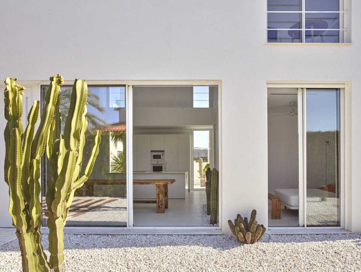 WHITE with white façade, two sliding glass doors, white gravel garden and tall columnar cactus in the foreground.