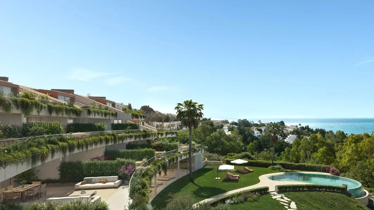 Project visualisation of CASATALAYA RESIDENCES with layered terraces full of greenery, palm trees, a lawn with sunbeds and an organically shaped swimming pond with sea visible on the horizon.