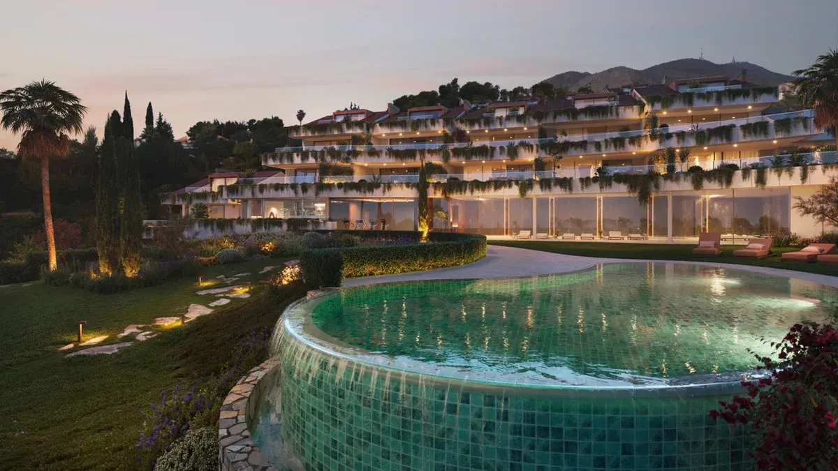 Evening visualization of CASATALAYA RESIDENCES with illuminated terraces, green façade planting, garden lighting and an organically shaped swimming pond with green mosaic tiles in the foreground.